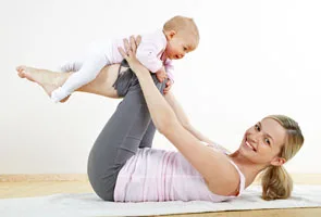 Mutter liegt auf einer Yogamatte und hält lachend ihr Baby über sich