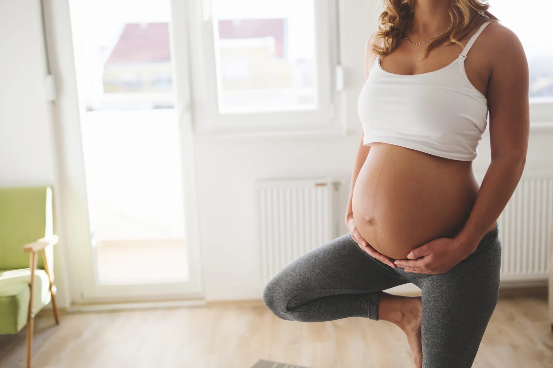 Schwangere in der Baumhaltung vor einem hellen Fenster, die Hände am Bauch